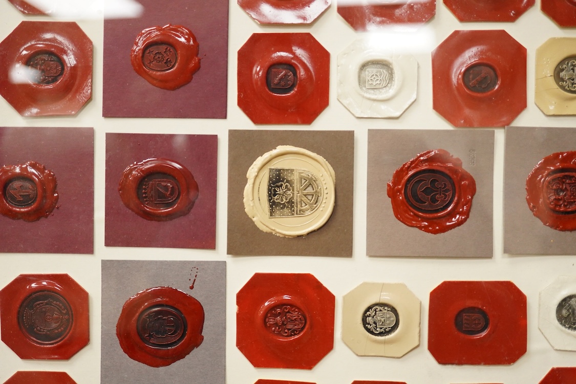 A framed display of red and white wax seals, some stamped Casolo Lausanne, 95 in total, 59cm wide